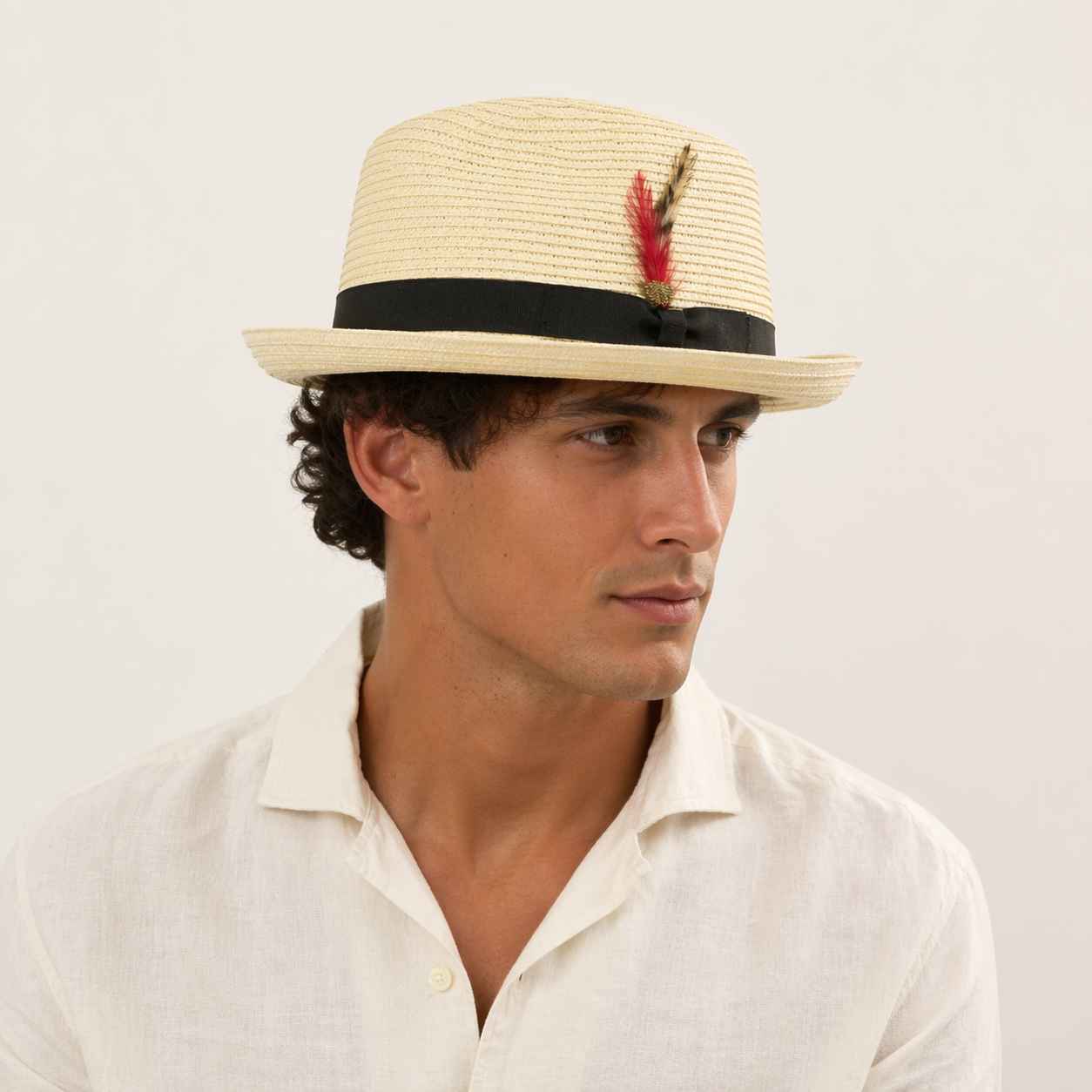 Man wearing a straw hat with a feather on a plain background